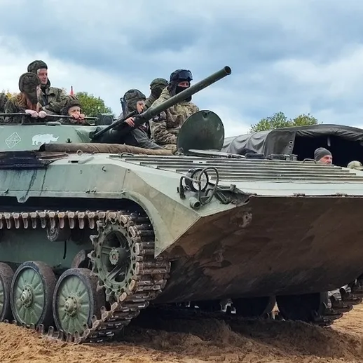 Много людей смотрят на танк, стоящий на земле в военной зоне в осенний день