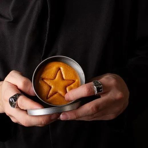 Мужчина в черной одежде держит жестяную коробку с печеньем в форме звезды на черном фоне