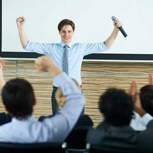 Успешный спикер презентует свою идею на конференции, поднимая руки в знак победы и восторга аудитории