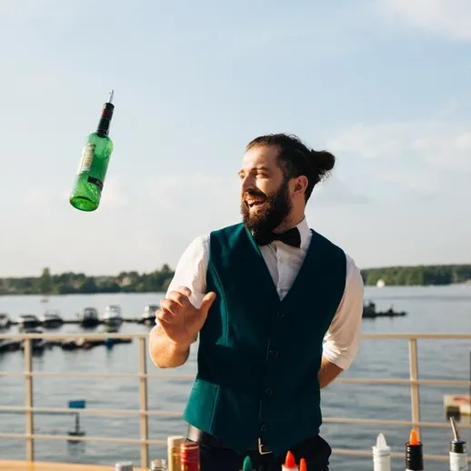 Бармен демонстрирует ловкость с бутылкой на фоне красивого водоема в теплый солнечный день