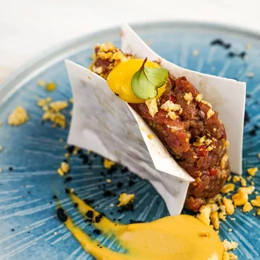 Нежный тартар из говядины с соусом и хрустящей посыпкой на синей тарелке