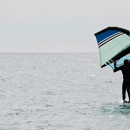 Серфингист на волнах океана в тёмный облачный день, демонстрирующий мастерство в кайтбординге