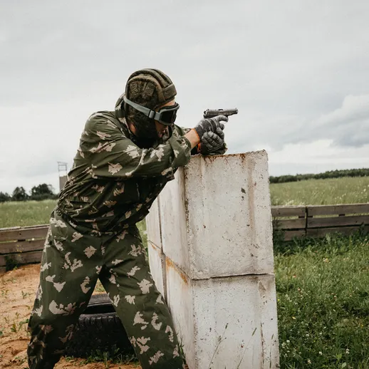 Профессиональный стрелок в камуфляже практикует стрельбу с пистолета на полигоне в солнечный день