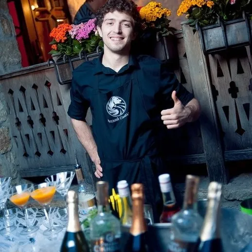 Улыбающийся бармен в ресторане на фоне цветов и напитков во время вечеринки