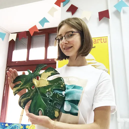 Девушка в светлой футболке держит зеленую фигуру растения в учебной комнате на арт-мастер-классе