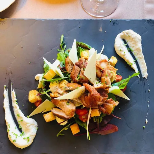 Элегантный салат с курицей и свежими овощами на черной тарелке в ресторане