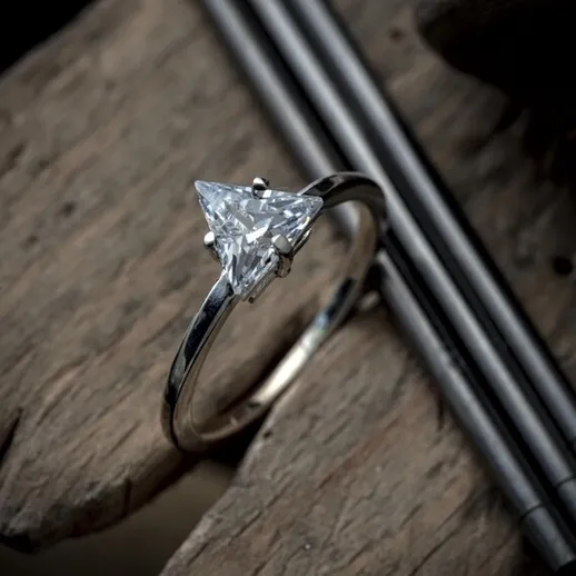 Уникальное обручальное кольцо с треугольным бриллиантом на фоне деревянного стола