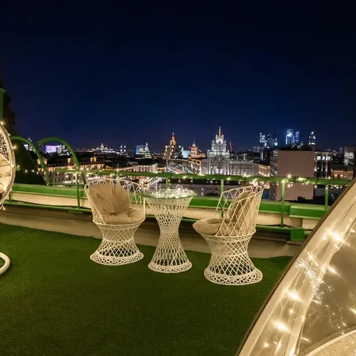 Уютная терраса с стильной мебелью, освещённая огнями, с видом на город в ночное время