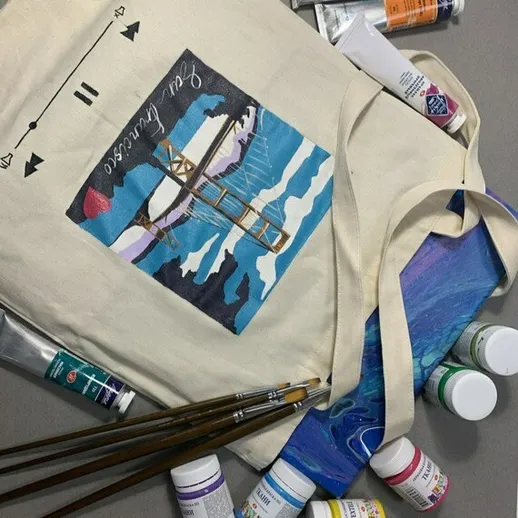 Сумка с художественным рисунком и кистями возле тюбиков краски на столе в студии художника