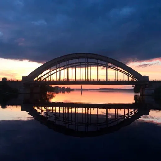 Мост на закате с отражением в реке, кадр с водной поверхности при вечернем свете, удаление от города
