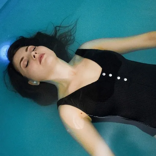 Женщина расслабляется, плавая в чистом голубом бассейне в спокойный день