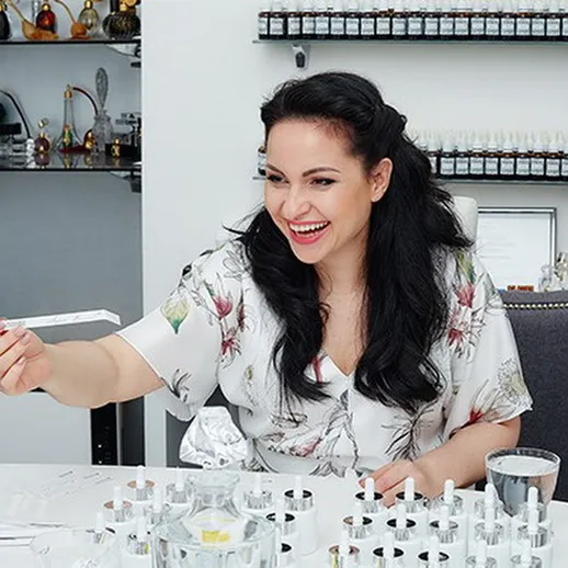 Женщина создает парфюм в лаборатории, окруженная флаконами и ингредиентами, в ярком помещении