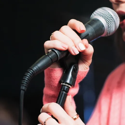 Молодая певица выступает на сцене, держит микрофон, одетая в розовый свитер в уютном клубе в вечернее время