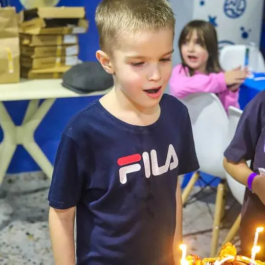 Мальчик радуется на дне рождения, задувая свечи на торте в магазине в вечернее время