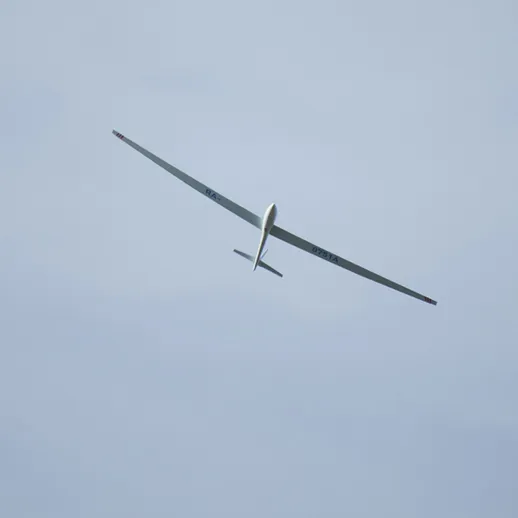 Летательный аппарат с длинным крылом взмывает в облачное небо над местностью