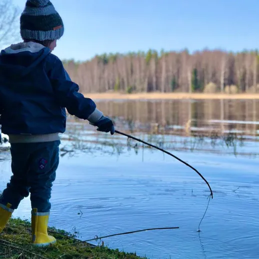 Ребёнок ловит рыбу с берега реки в ясный день ранней весны