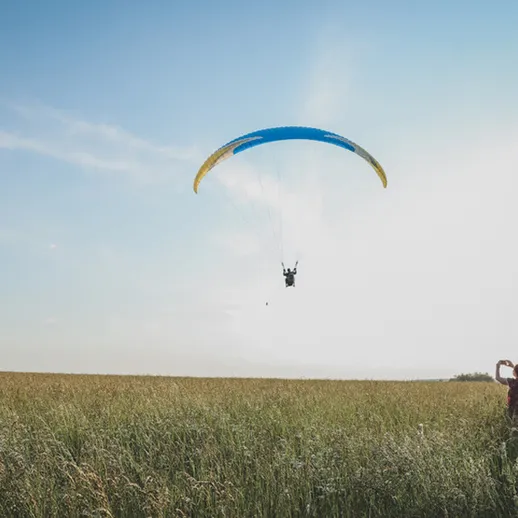 Парапланерист приземляется на поле в солнечный день, наслаждаясь свободным полетом в живописной местности