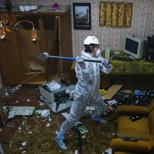 В разрушенной комнате человек в защитном костюме готовится разбить предметы