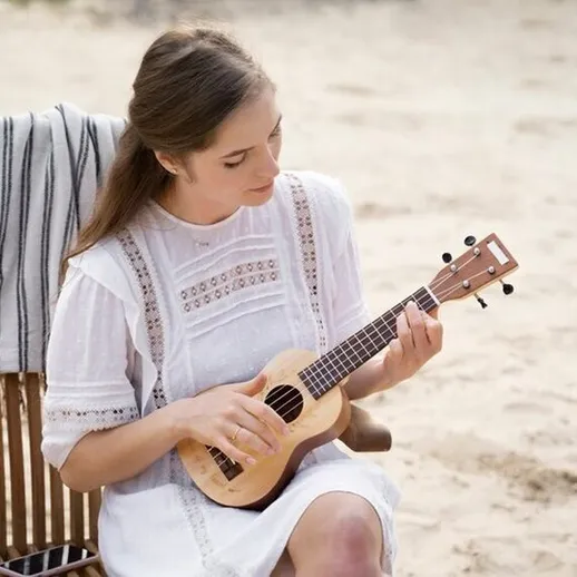 Женщина играет на укулеле на пляже в теплый день