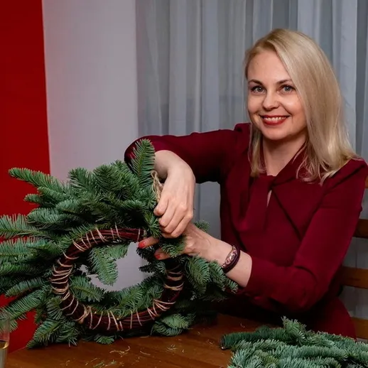 Женщина создает новогодний венок из еловых веток в уютном интерьере