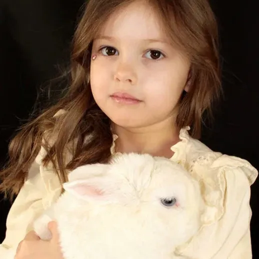 Девочка с длинными волосами нежно держит белого кролика на черном фоне в уютной атмосфере