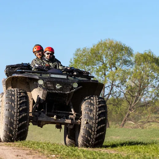 Квадроцикл едет по дороге в живописной местности в солнечную погоду, двое людей наслаждаются активным отдыхом