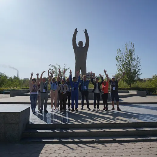 Группа людей в поднятых руках на фоне памятника, парк, солнечный день, местность в России
