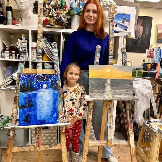 Девушка и ребёнок позируют с картинами на мольбертах в художественной студии, вечерняя атмосфера, уютная обстановка