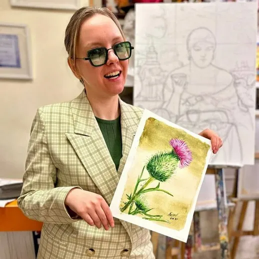 Художница демонстрирует акварельную работу с цветком чертополоха в художественной студии