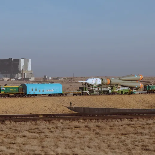 Поезд с ракетой на платформе проезжает мимо космического комплекса в пустыне