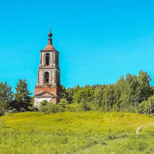 Звонница старой церкви на фоне синего неба и зелёной травы в летний день