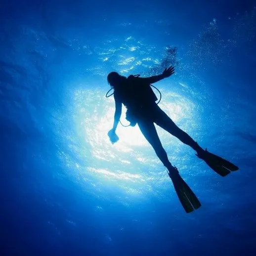 Плавание дайвера под водой в ярком свете на глубине океана в тропической местности
