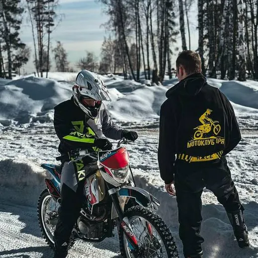 Мотоциклист в зимнем лесу на фоне заснеженных деревьев и яркого неба в солнечный день