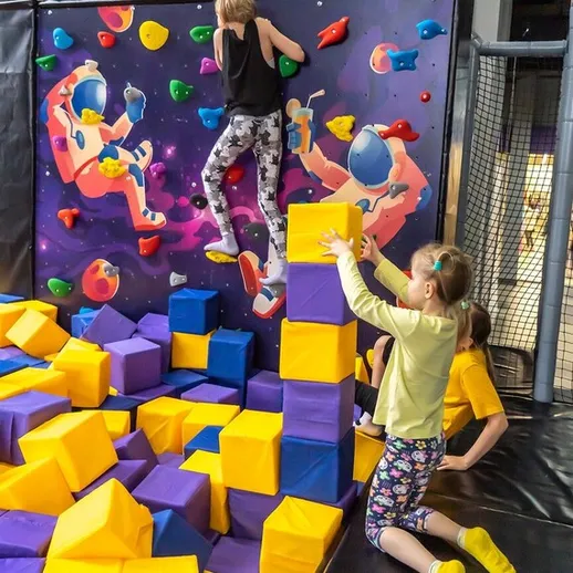 Дети занимаются скалолазанием в развлекательном центре на фоне яркой графики в вечернее время