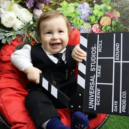 Маленький актер с клиппаром на фоне цветов и картона в уютном уголке