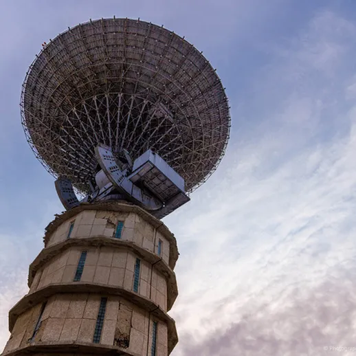 Антенна с параболическим зеркалом на фоне облачного неба в районе города