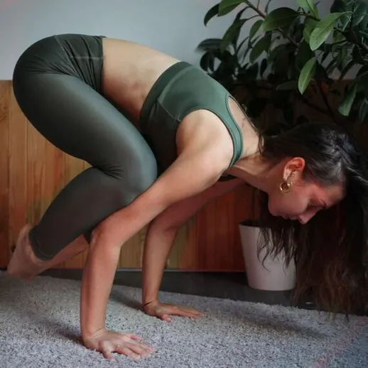 Женщина выполняет сложную асану йоги в домашних условиях на подстилке из мягкого материала