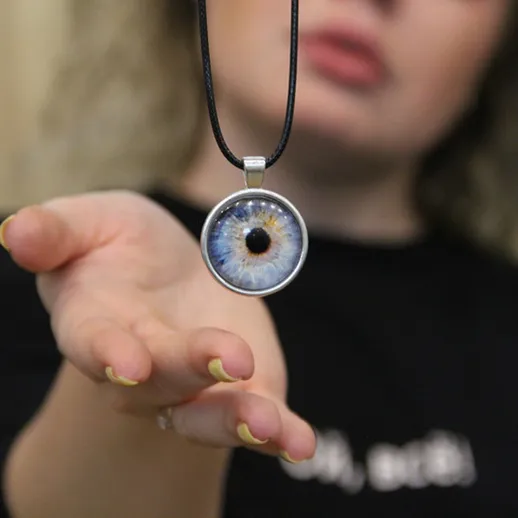 Женщина держит подвеску с глазом, демонстрируя детали, на фоне уютного интерьера