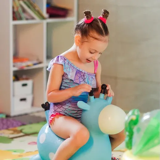 Девочка играет на синем козлике в детской комнате во время занятия