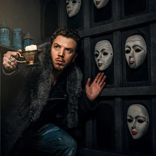 Мужчина с кружкой в руке стоит в темной комнате с масками на стене, исследуя загадочную атмосферу около полуночи