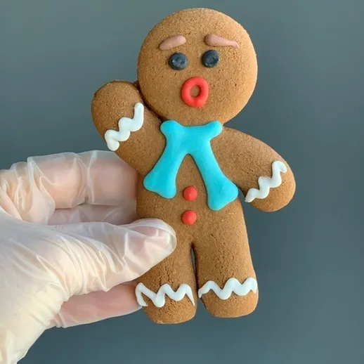 Имбирный человечек с яркой глазурью на фоне серой поверхности, который держит руку поднятой и выглядит радостно