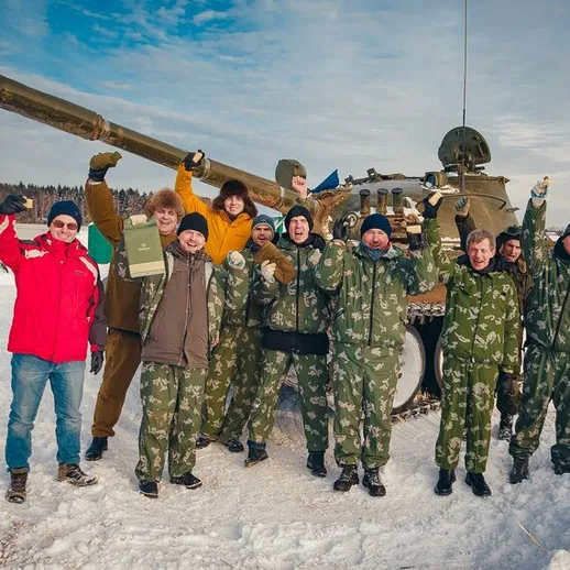 Ряд солдат и гражданских лиц позируют у танка на заснеженной местности в светлое зимнее время