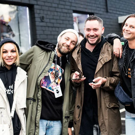 Четыре молодых человека улыбаются и позируют на улице в больших пальто