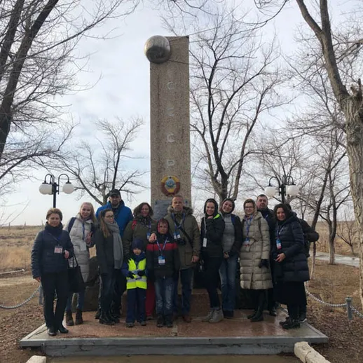 Группа людей у памятника в открытой местности в холодную погоду, ужасные деревья вокруг и хмурое небо