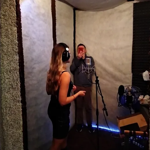 Запись песни в студии звукозаписи, девушка поет в наушниках, а парень снимает на телефон
