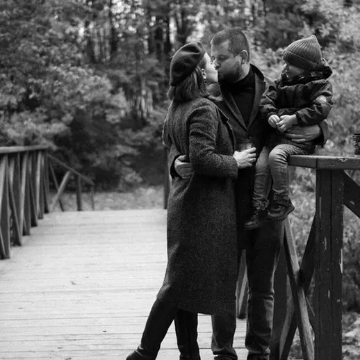 Семейная прогулка по мосту в осеннем лесу, мама и папа обнимаются, а ребенок весело смотрит