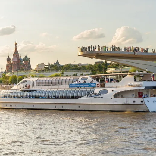 Корабль движется по Москве-реке, мимо исторических зданий и людей на набережной в летний день
