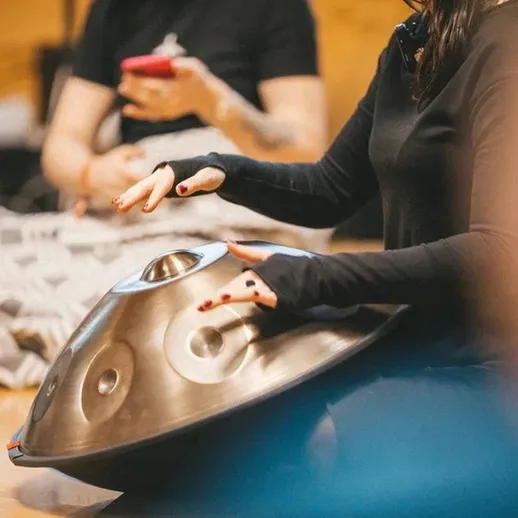 Игрок на хэндпан играет мелодию в кругу людей на занятии по музыке в уютном помещении