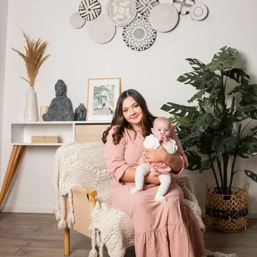 Мать с младенцем на диване в уютном интерьере с зелеными растениями и декоративными элементами