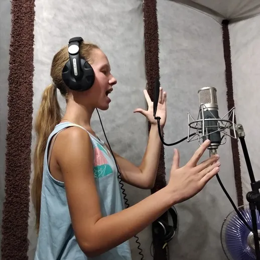 Девочка поет в звукозаписывающей студии, используя микрофон и наушники, вечернее время